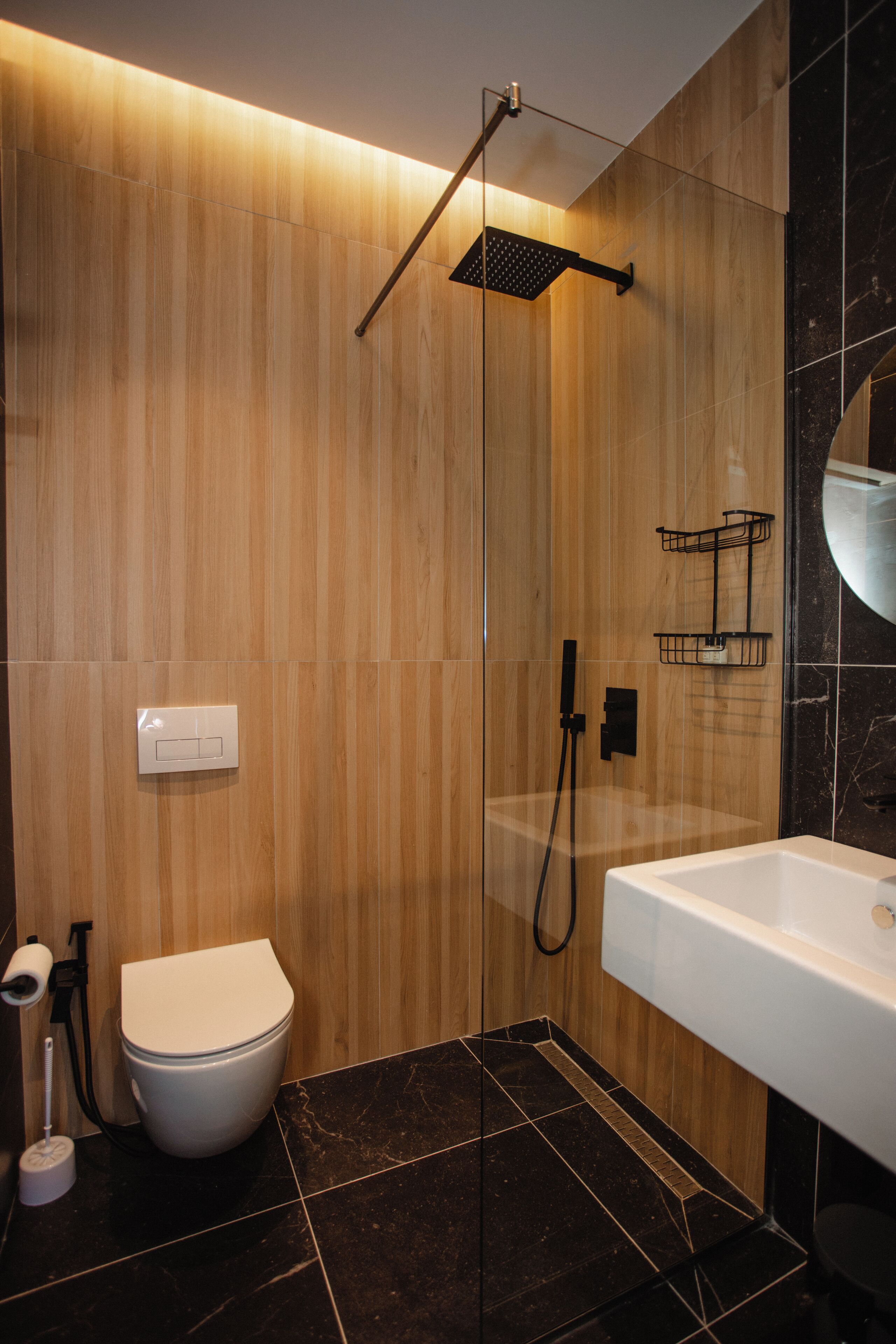 A modern bathroom with a wooden wall, a white toilet, a black shower, and a white bathtub.
