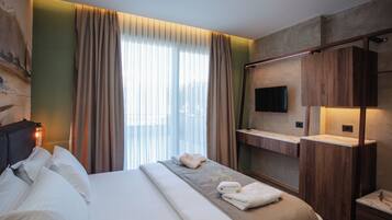 Une chambre d’hôtel moderne dotée d’un grand lit, d’un téléviseur à écran plat fixé au mur, d’une coiffeuse en bois et d’une grande fenêtre avec des rideaux.
