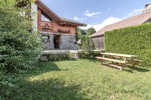 Situated in a lush garden, this charming cabin features a wooden door and windows, a stone wall, and a picnic table for outdoor dining or relaxation.