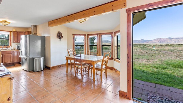 A kitchen with a dining table, wooden ceiling beams, and a view of a grassy field through large windows. - Peggy s View - Uplifting Cozy Mountain Views (Alpine)