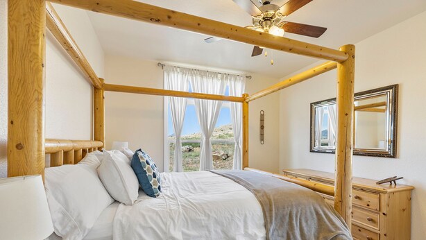 Un lit à baldaquin avec une literie blanche, une commode en bois, un miroir et une fenêtre avec des rideaux.