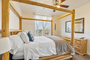Un lit à baldaquin avec une literie blanche, une commode en bois, un miroir et une fenêtre avec des rideaux.