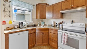 Une cuisine avec des meubles de rangement en bois, un lave-vaisselle, une cuisinière et une fenêtre avec un rideau.