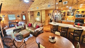 A wooden cabin interior with a living room, dining area, and kitchen. - BEAR CROSSING - HOT TUB, GAME ROOM, SECLUDED (Helen)