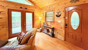 A wooden cabin interior with a couch, a lamp, a door with a frosted glass window, and a welcome sign. - BEAR CROSSING - HOT TUB, GAME ROOM, SECLUDED (Helen)
