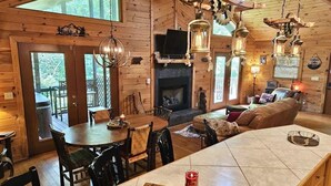 A cozy cabin interior with a fireplace, wooden walls, a dining area, and a living room with a sofa. - BEAR CROSSING - HOT TUB, GAME ROOM, SECLUDED (Helen)