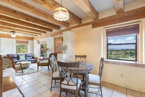A spacious living room with a wooden ceiling, a round dining table with chairs, a sofa, and a view through a window. - Adobe Vista - Cozy and Inviting Spectacular View (Alpine)