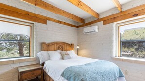 Ein Schlafzimmer mit einem hölzernen Kopfende, einem Bett mit weißer Bettwäsche, einem Nachttisch und einem Fenster mit Blick auf Bäume.