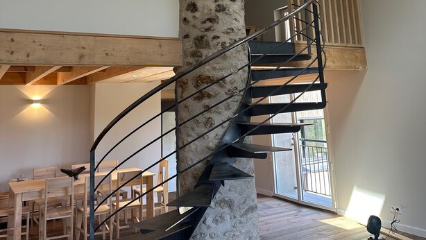 A spiral staircase with a stone pillar, wooden beams, and a skylight.