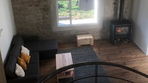A cozy living room with a stone wall, a black sofa, a small wooden table, a fireplace, and a skylight.
