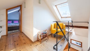A loft bedroom with a wooden floor, a yellow chair, a bed with a purple headboard, and a skylight. - Spacious 2-level apart National Theatre (Prague)