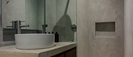 A modern bathroom with a large mirror, a white sink, a shower, and a small window.