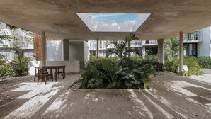 An outdoor patio area with a concrete ceiling, a table and chairs, and a planter with large leafy plants. - Seremonia Selva (Tulum)
