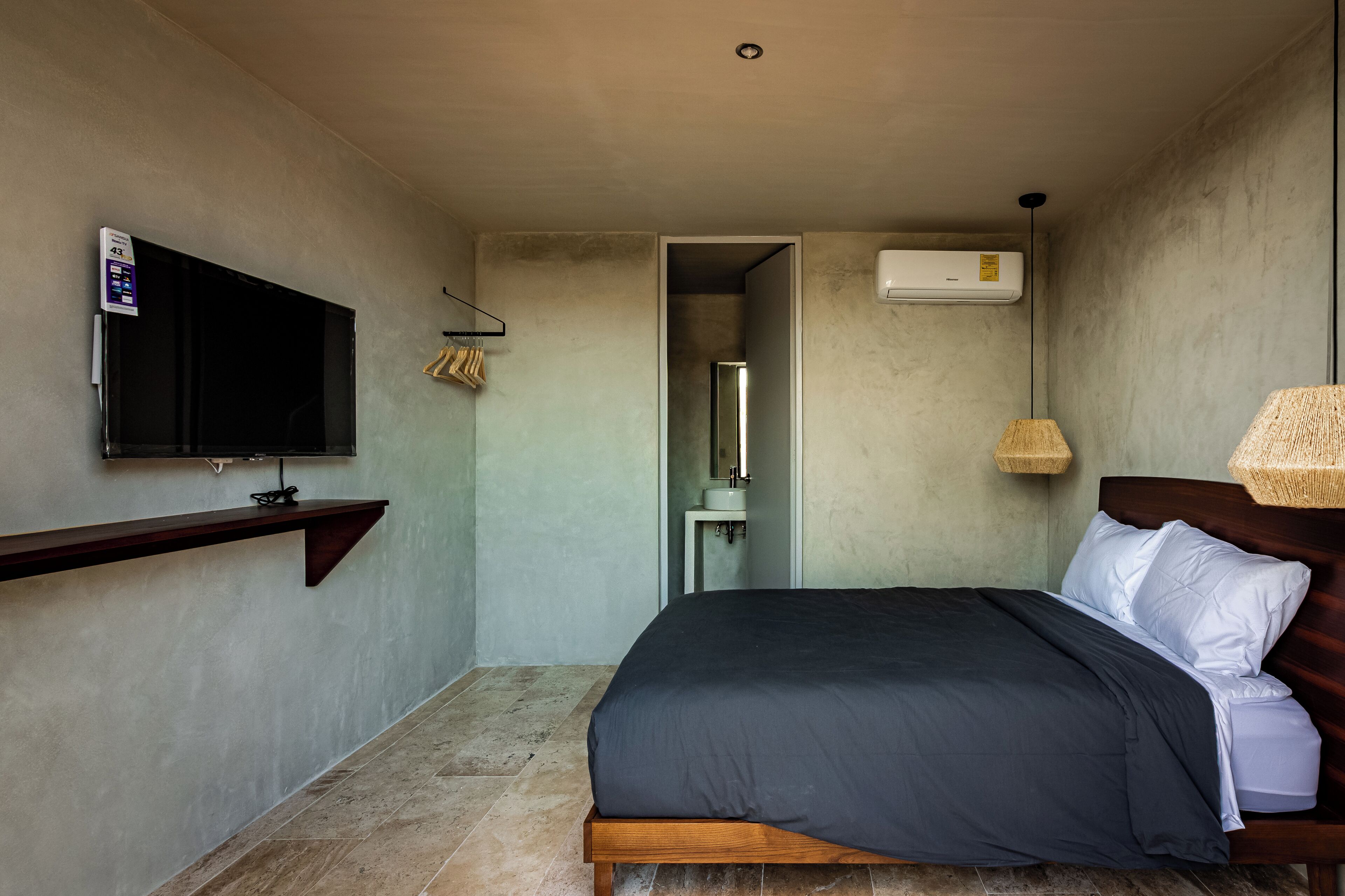 A bedroom with a bed, a TV mounted on the wall, a bedside lamp, and an air conditioning unit.