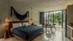 A modern bedroom with a large bed, a dining area with chairs, and a balcony with a view of greenery. - Seremonia Selva (Tulum)