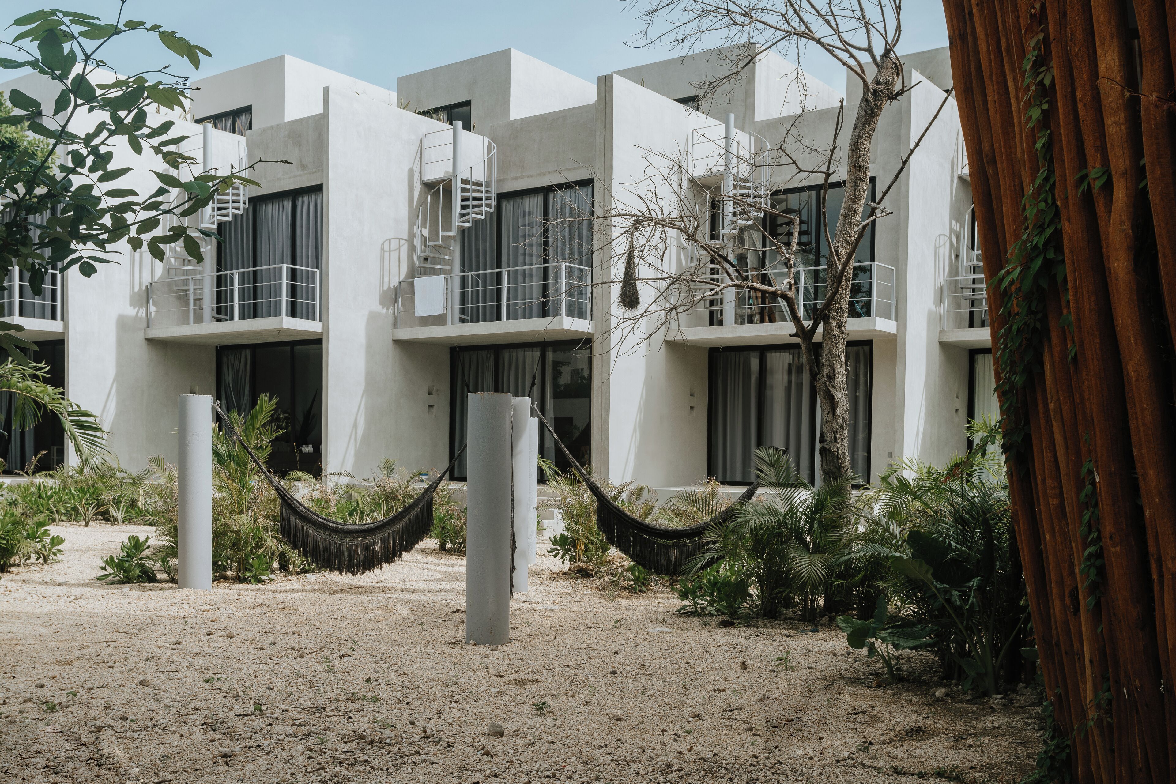 A modern building with multiple balconies, a hammock, and a sandy ground.