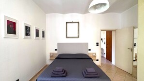 Ein Schlafzimmer mit Bett, Nachttisch, Pendelleuchte und gerahmten Bildern an der Wand.
