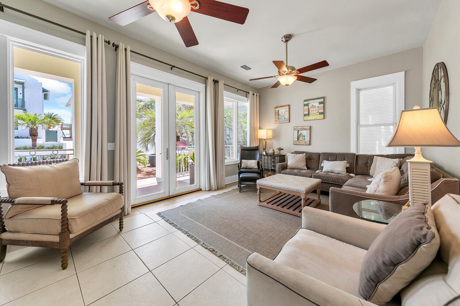 A spacious living room with a sofa set, a coffee table, and a TV. There are two ceiling fans, a lamp, and a window with curtains.