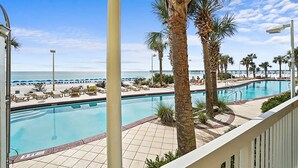A pool area with palm trees, lounge chairs, and a view of the beach. - ☀️BeachFront-Pools-Tiki Bar-Calypso 2-103☀️ (Panama City Beach)