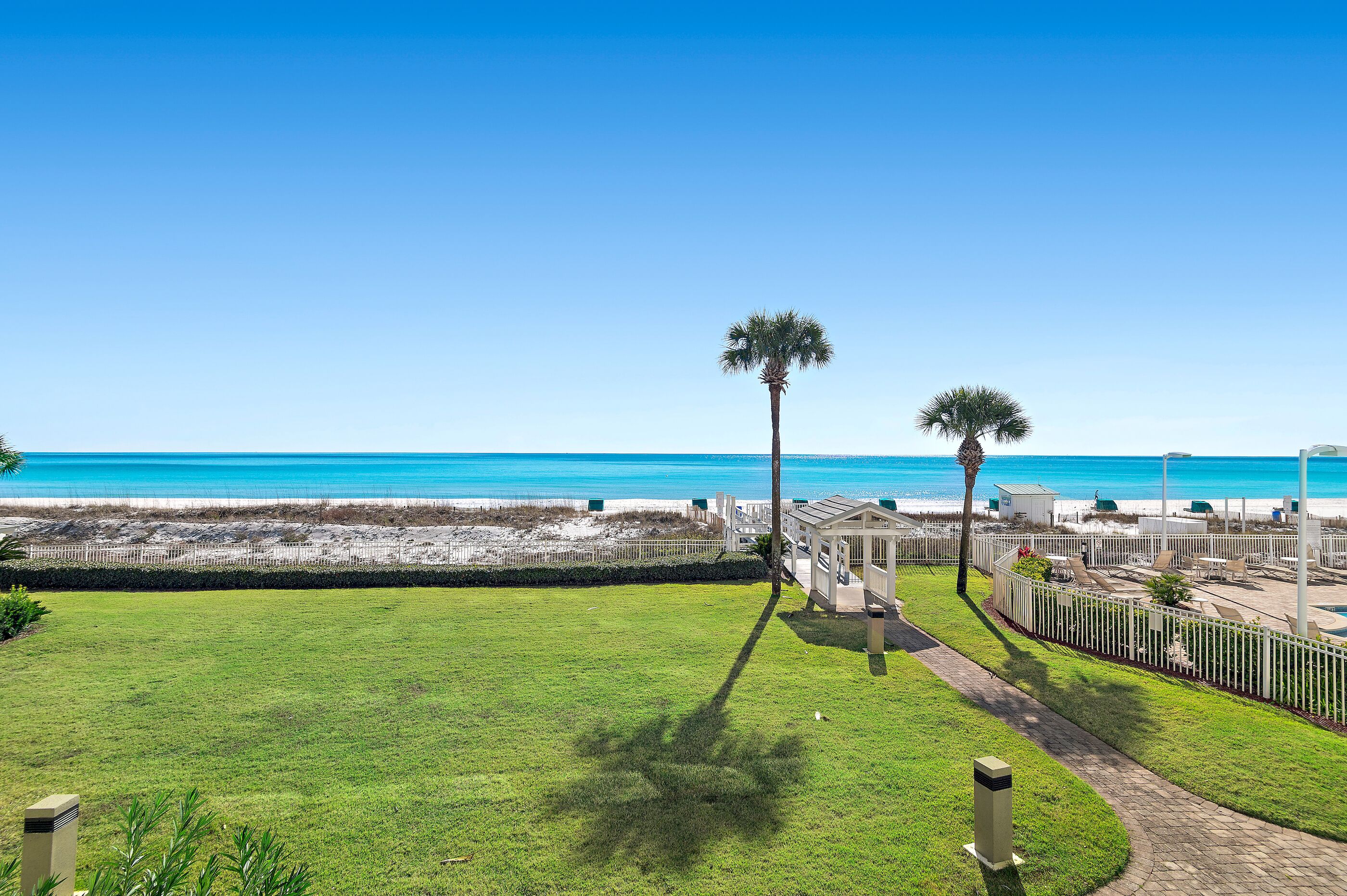 A beachfront property with a grassy lawn, a pathway, and a view of the ocean.
