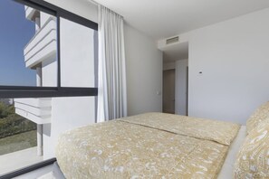 Ein Hotelzimmer mit großem Fenster, einem Bett mit gemusterten Textilien und Blick ins Freie.