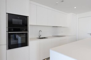 A modern kitchen with white cabinetry, a double oven, a stainless steel sink, and a countertop.