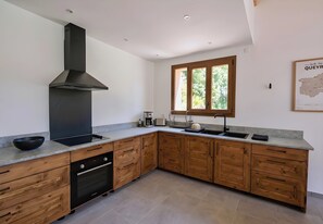 Une cuisine moderne avec des meubles en bois, une hotte noire, un four encastré et une fenêtre donnant sur un paysage verdoyant.