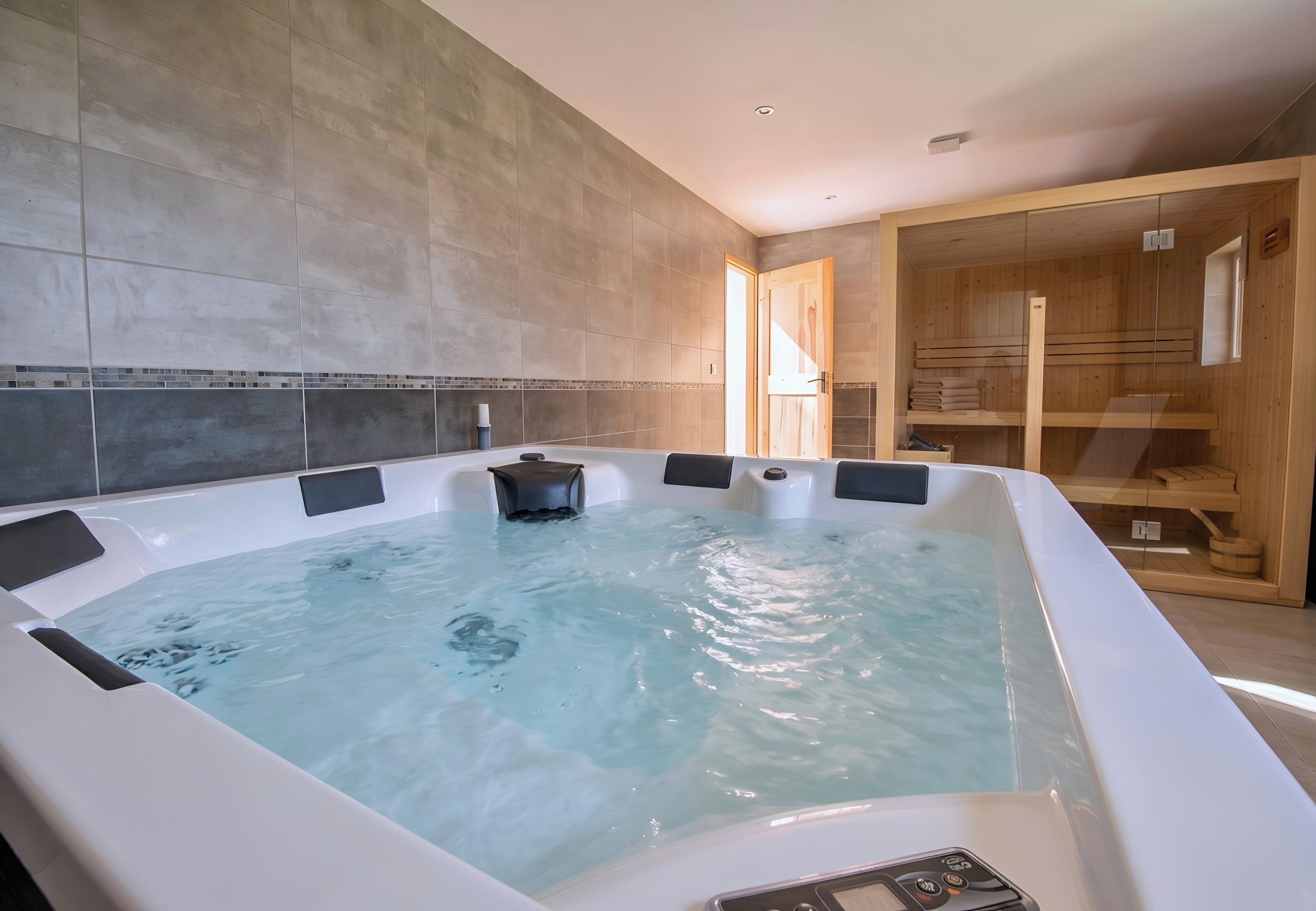 A hot tub with a control panel, tiled walls, and wooden shelving.