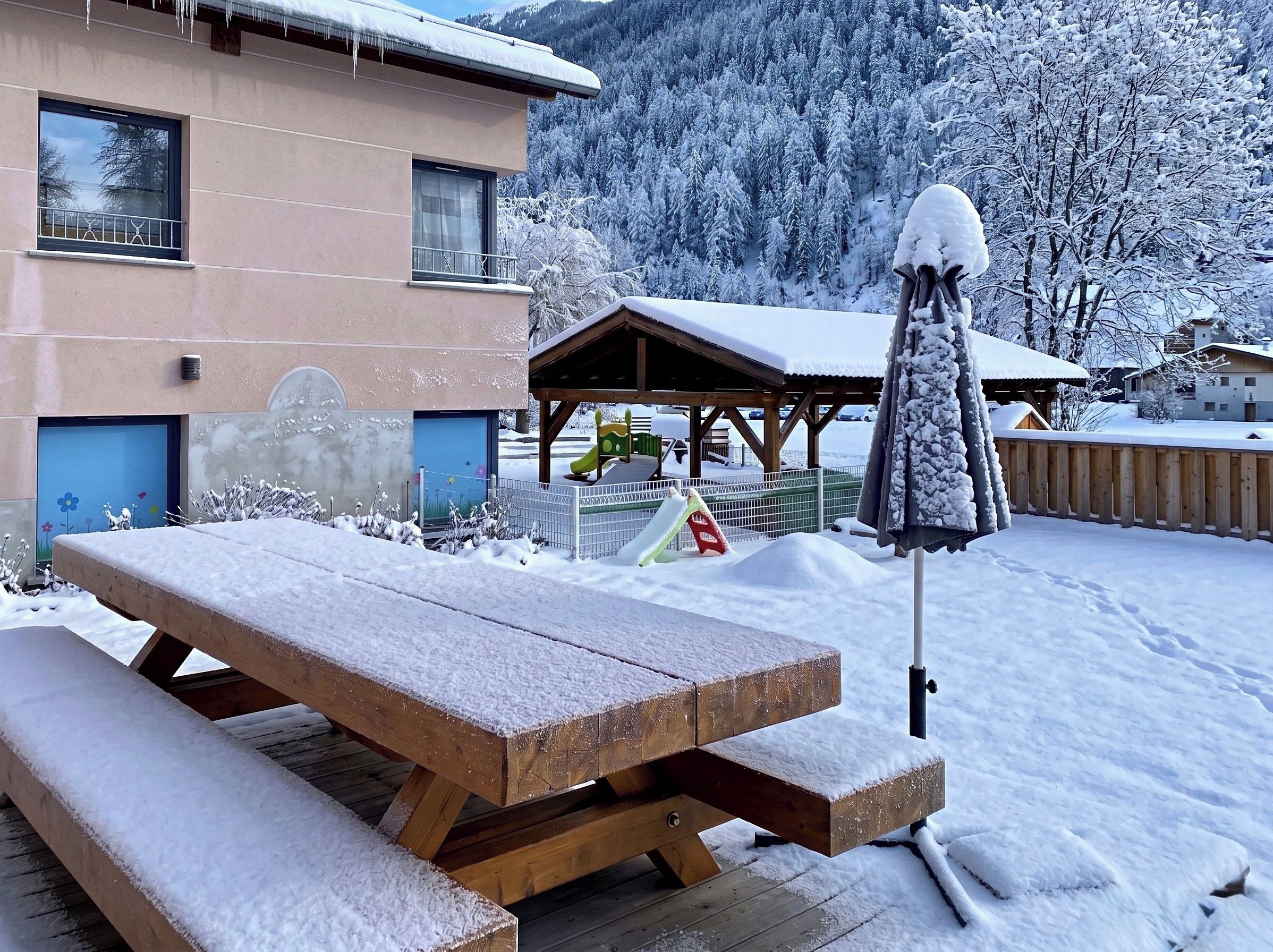 A wooden picnic table and a covered seating area in a snowy outdoor setting.