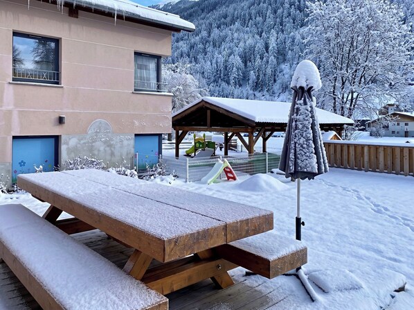 Una mesa de picnic de madera y un área de estar techada en un paisaje invernal nevado.