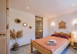 A bedroom with a wooden bed, a wall-mounted mirror, a vase with pampas grass, and a wooden nightstand with a lamp.