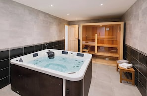 A modern bathroom with a large bathtub, a wooden sauna, and a small bench with towels.