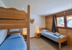 Una habitación con dos literas de madera, una mesita de noche con lámpara, una ventana con cortinas y vistas al exterior.