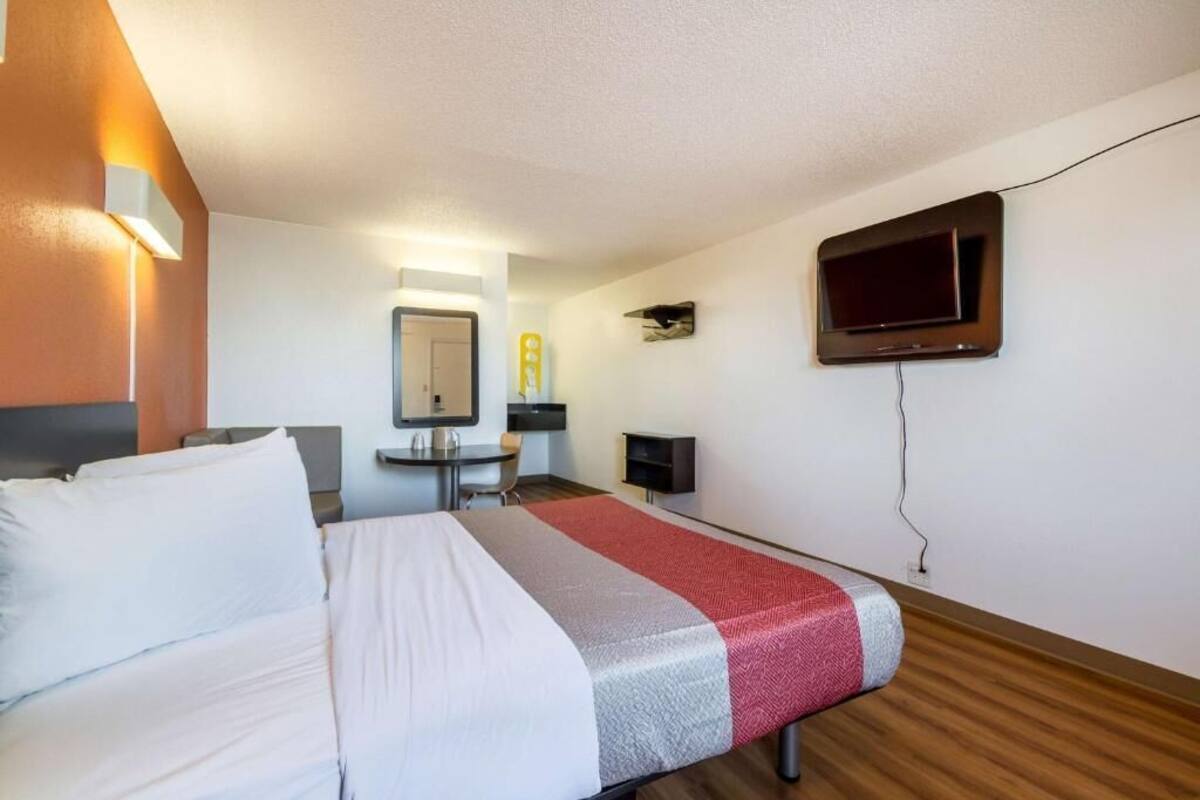 Una habitación de hotel con cama, escritorio, silla, televisión y una pequeña mesa con lámpara.