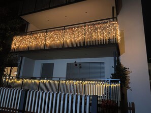 A building with a balcony adorned with string lights, a white exterior, and a metal railing.
