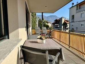 Ein Balkon mit Tisch und Stühlen, einer Blumenvase und Blick auf Gebäude und Berge.
