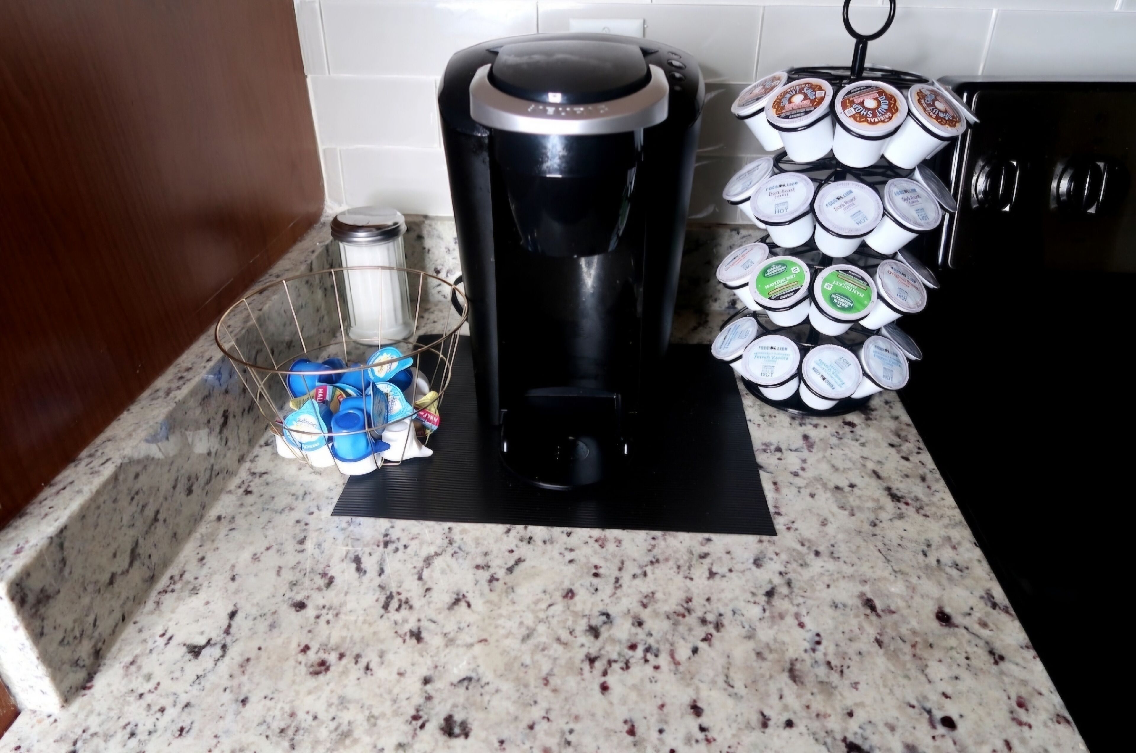 A kitchen counter with a coffee maker, a basket of coffee pods, and a stack of yogurt containers.