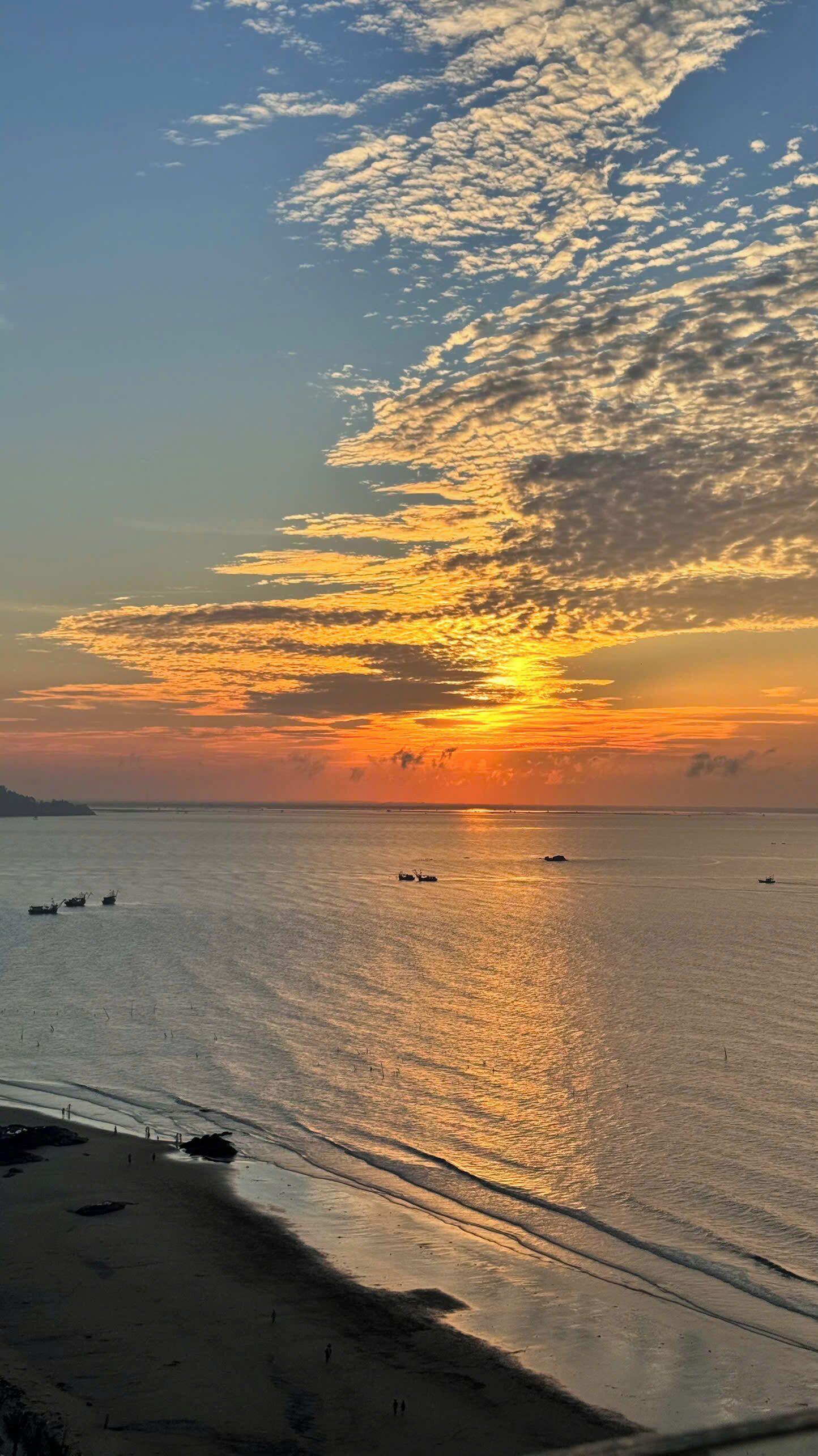 A beach with a sunset, calm sea, and boats.