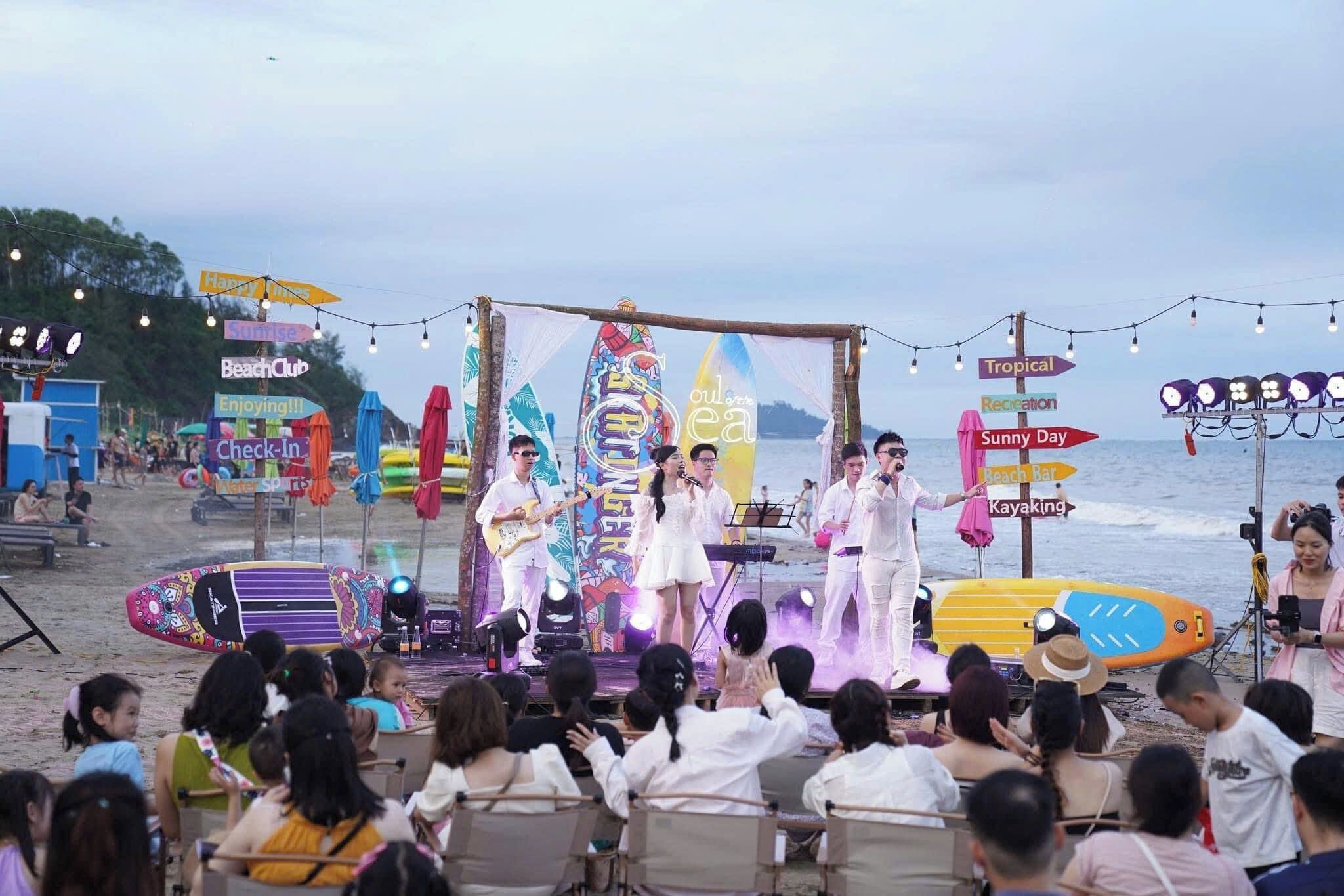 Um palco na praia com uma banda tocando, cercado por pessoas.