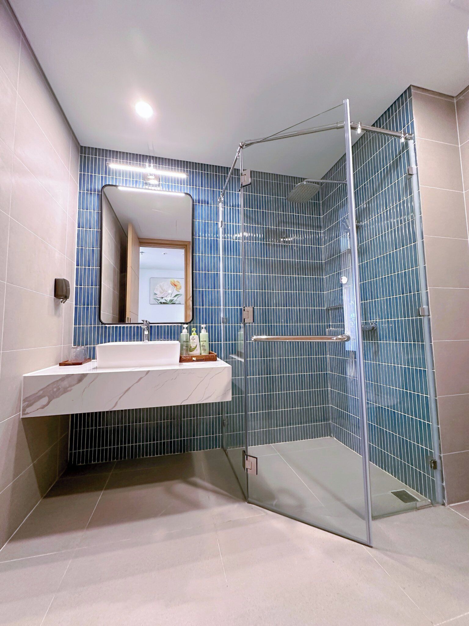 A modern bathroom with a glass-enclosed shower, a marble sink, and blue-tiled walls.
