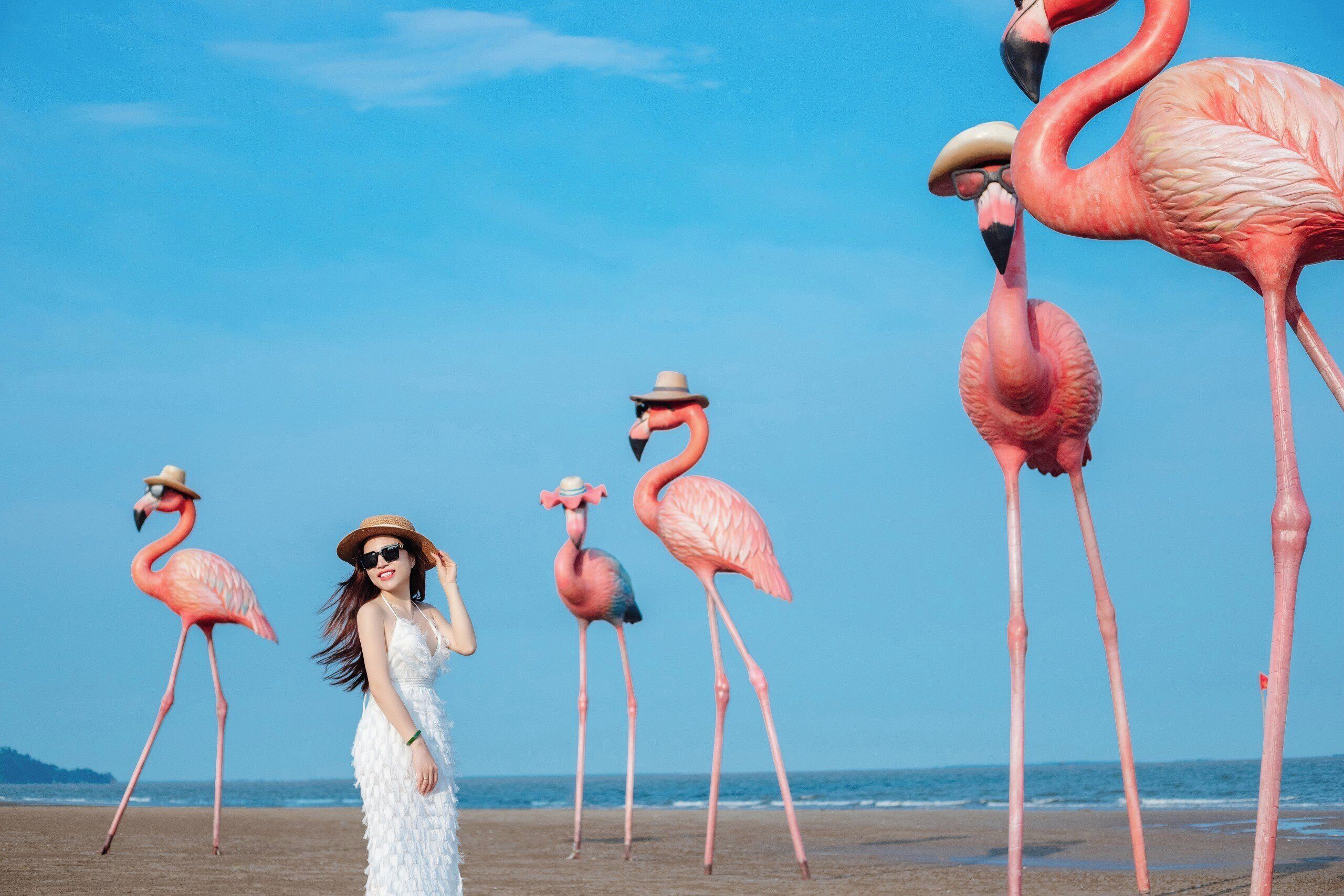 A beach with a woman in a white dress and a straw hat, surrounded by pink flamingos.