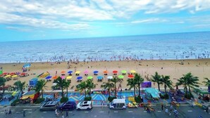 A beach with people, umbrellas, and palm trees. - Flamingo Hai Tien  (Hoang Tien)