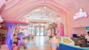 A brightly lit ice cream shop with a pink and white color scheme, a large glass entrance, and a counter with a display case. - Flamingo Hai Tien  (Hoang Tien)