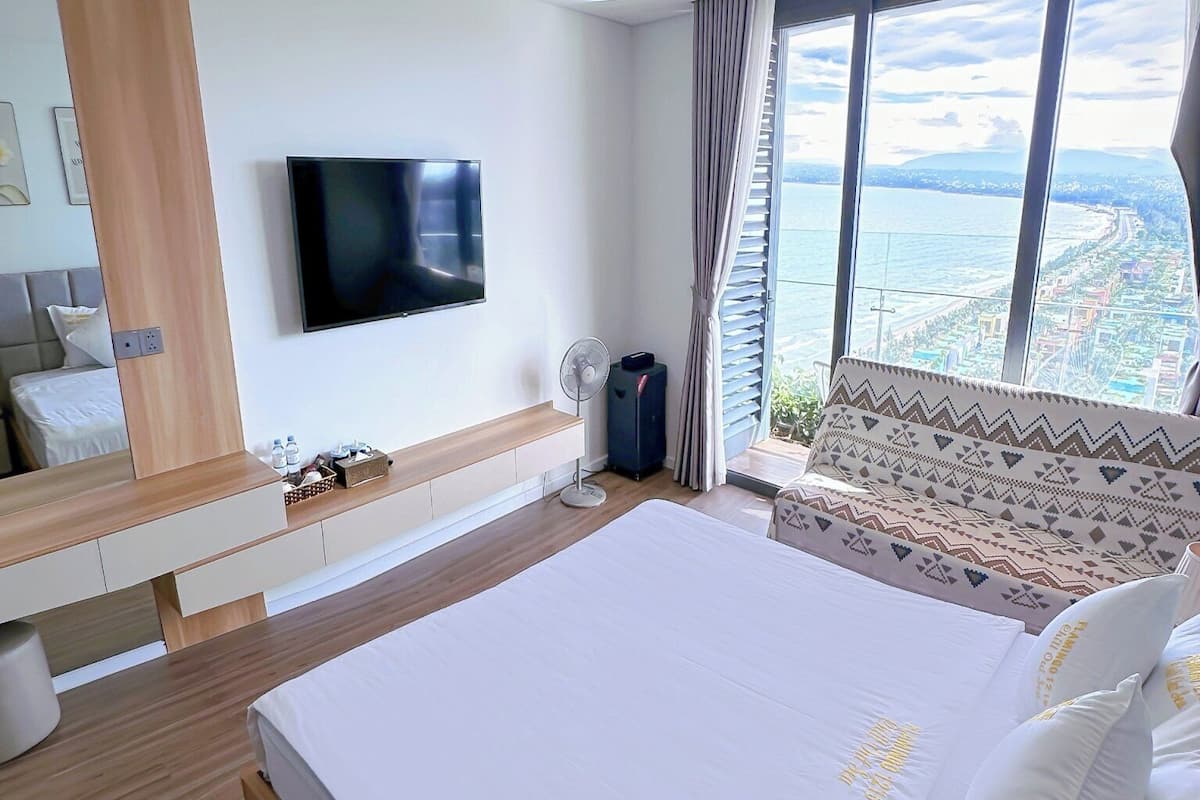 Une chambre d’hôtel moderne avec un grand lit, un téléviseur fixé au mur, une vue sur la mer et un plancher en bois.