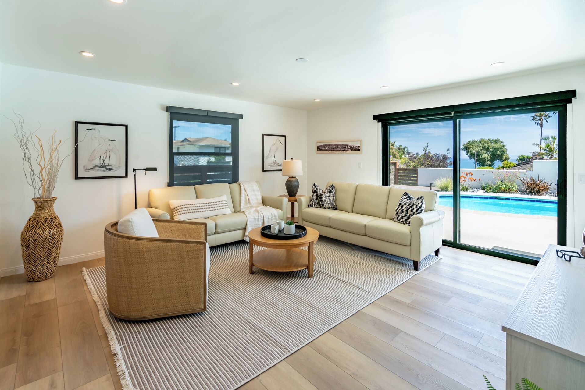 A spacious living room with a large window, a sofa, a coffee table, and a wicker chair.