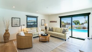 Un salon spacieux avec une grande fenêtre, un canapé, une table basse et un fauteuil en osier.