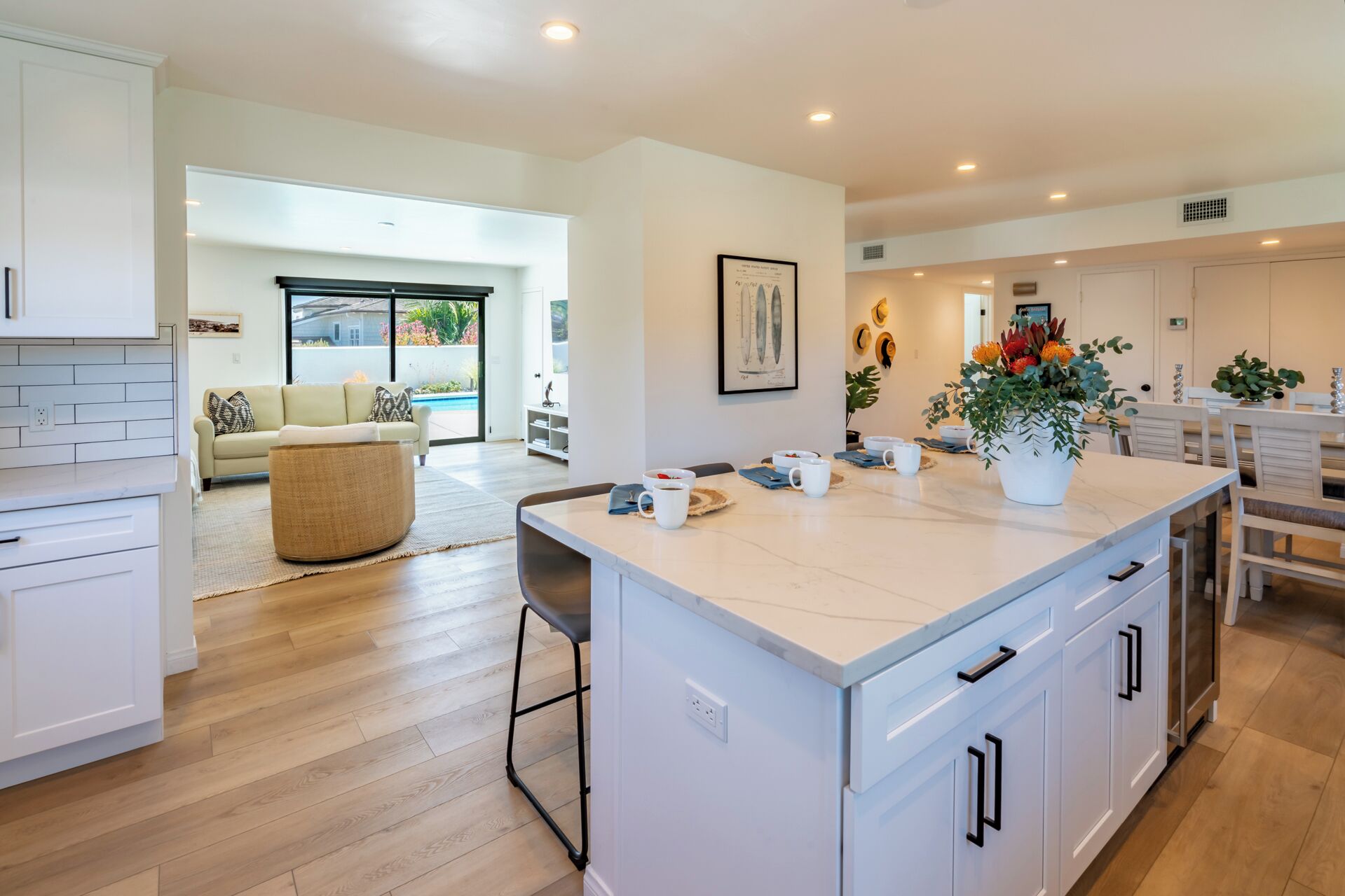 A modern kitchen with white cabinetry, a central island, and a dining area with white chairs.
