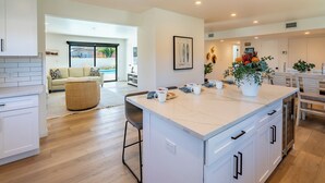 Une cuisine moderne avec des meubles blancs, un îlot central et un coin repas avec des chaises blanches.