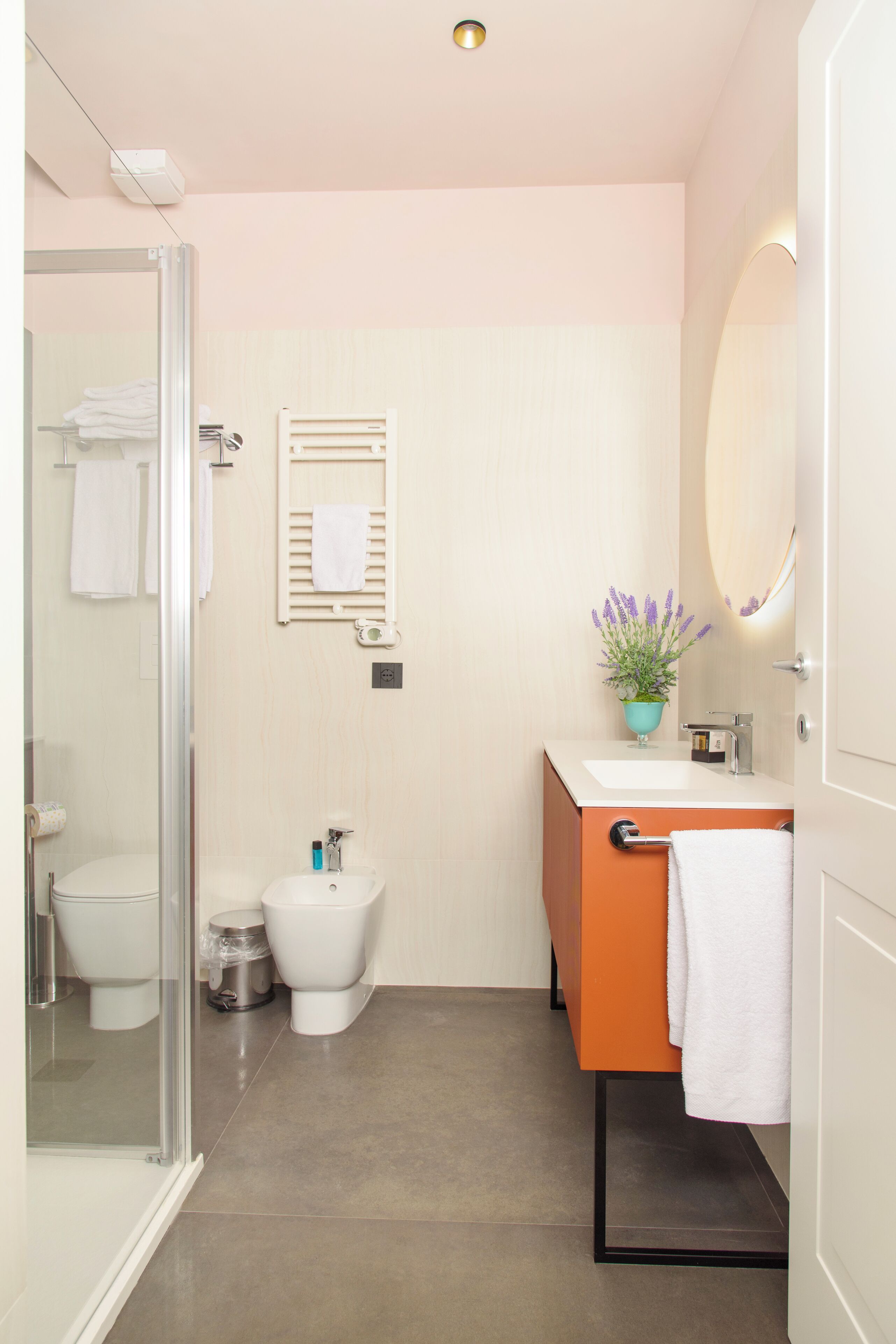 A modern bathroom with a glass shower enclosure, a white toilet, and an orange vanity with a mirror.