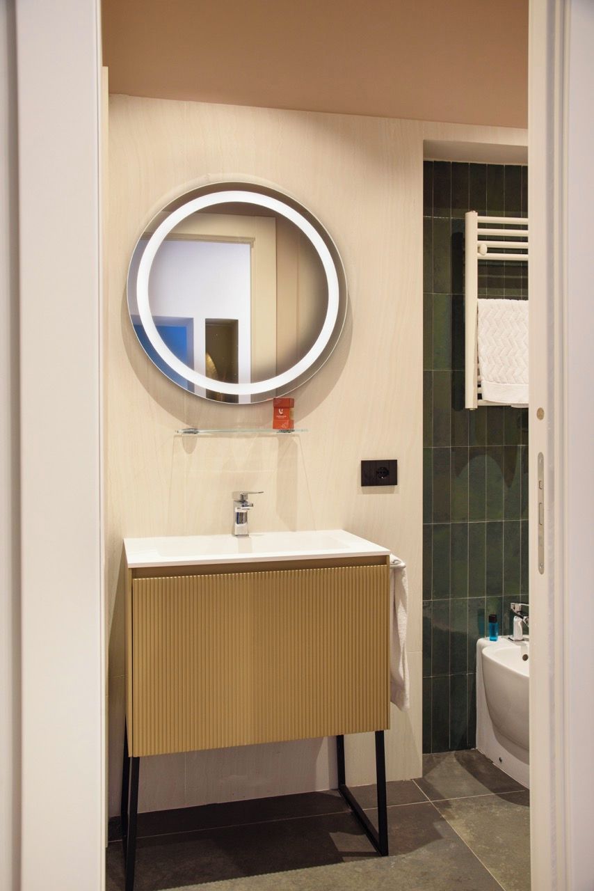 A bathroom with a round mirror, a white sink, a towel rack, and a bathtub.